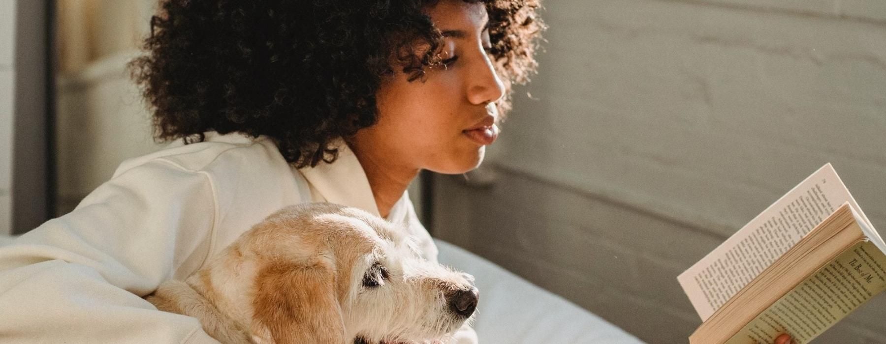 a person reading a book while laying next to a dog