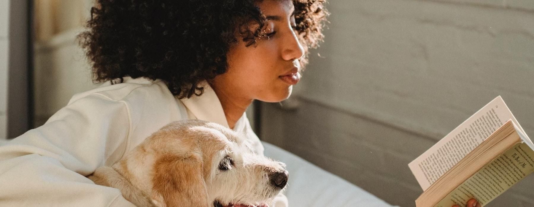 a person reading a book while laying next to a dog